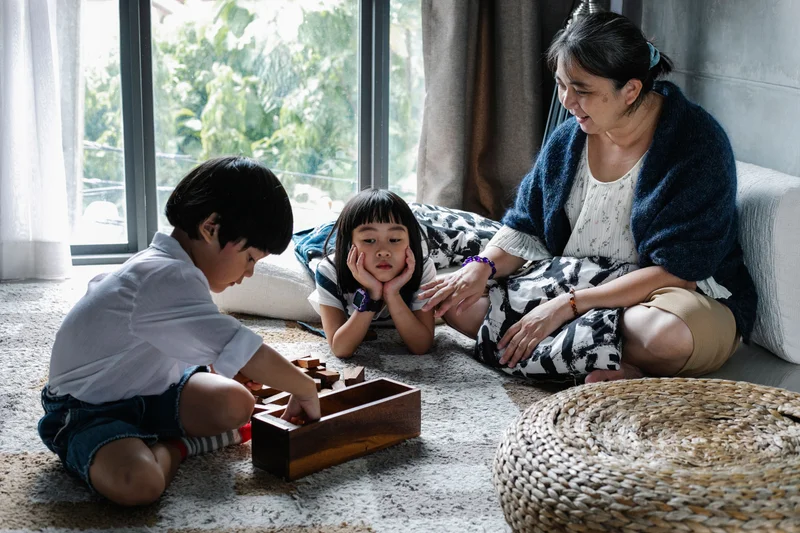 Grandmother watching two grandchildren play a wooden puzzle game together