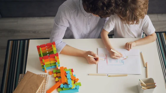 A parent and child drawing together at a table with coloured pencils