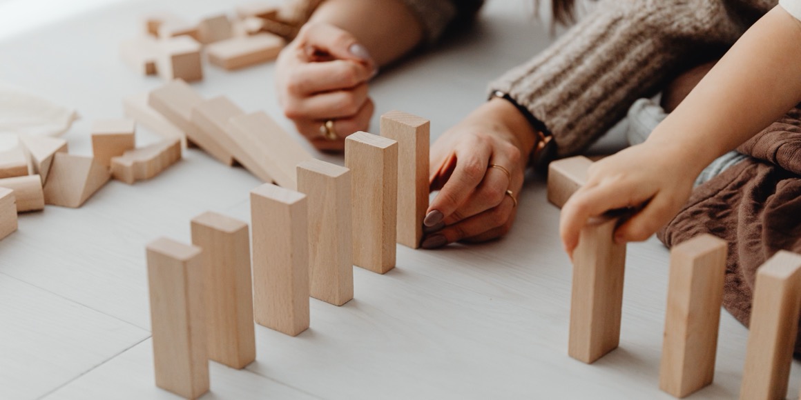 Adult hands arranging wooden blocks on a pale floor, mid-activity